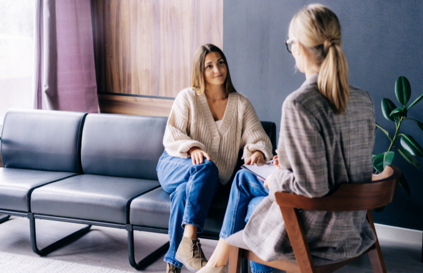 Mujer joven en consulta psicológica con una terapeuta profesional, en un consultorio moderno y acogedor. Imagen representativa para ilustrar cuánto cuesta un psicólogo en México en sesiones presenciales.