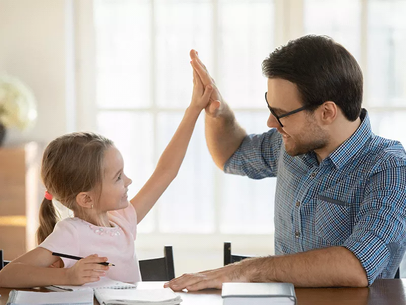 Papá con camisa de cuadros azul y lentes chocando palmas para celebrar con su hija rubia de playera rosa en un ejemplo de disciplina positiva