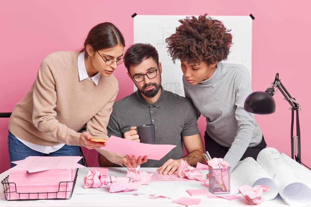 Foto de una oficina color rosa con un grupo de tres adultos trabajando haciendo uso de sus habilidades blandas